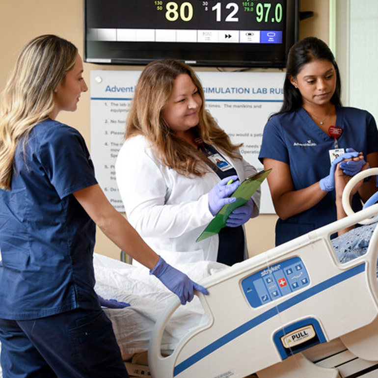 Two female nurse residents working with a female physician as they care for a patient in a hospital bed