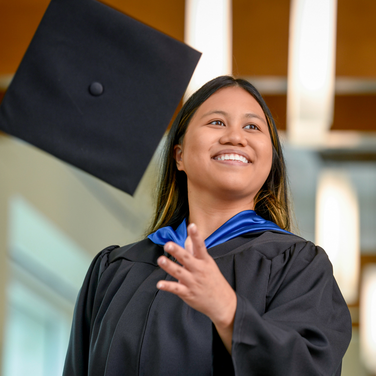 A smiling female nursing student graduating and throwing her cap in the air