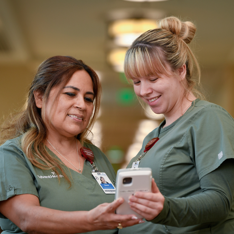 Two smiling female environmental services workers collaborating in a hospital setting