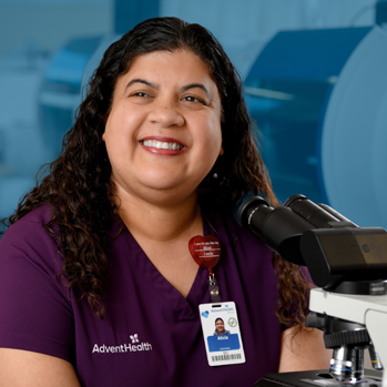 A smiling female laboratory technician in front of a microscope