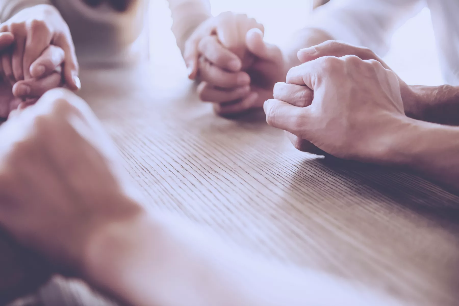 A group of friends holds hands in prayer.