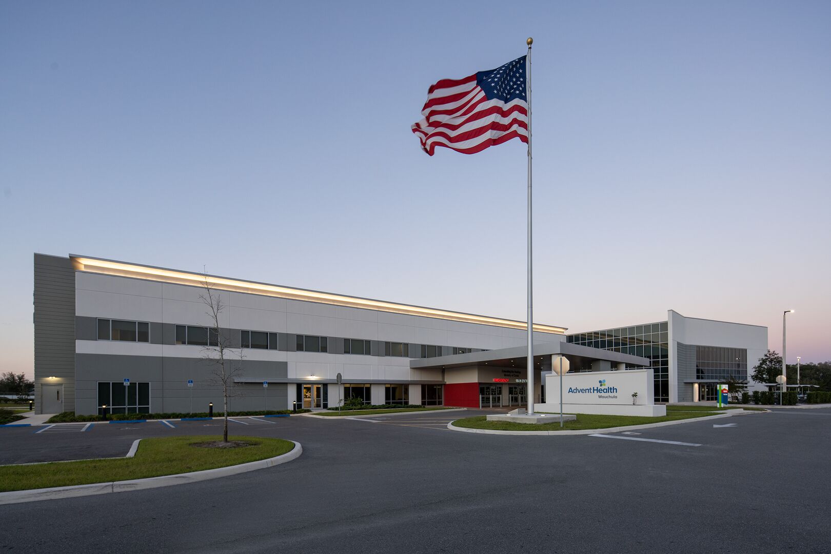 Exterior of AdventHealth Wauchula hospital at dusk with U.S. flag in foreground.