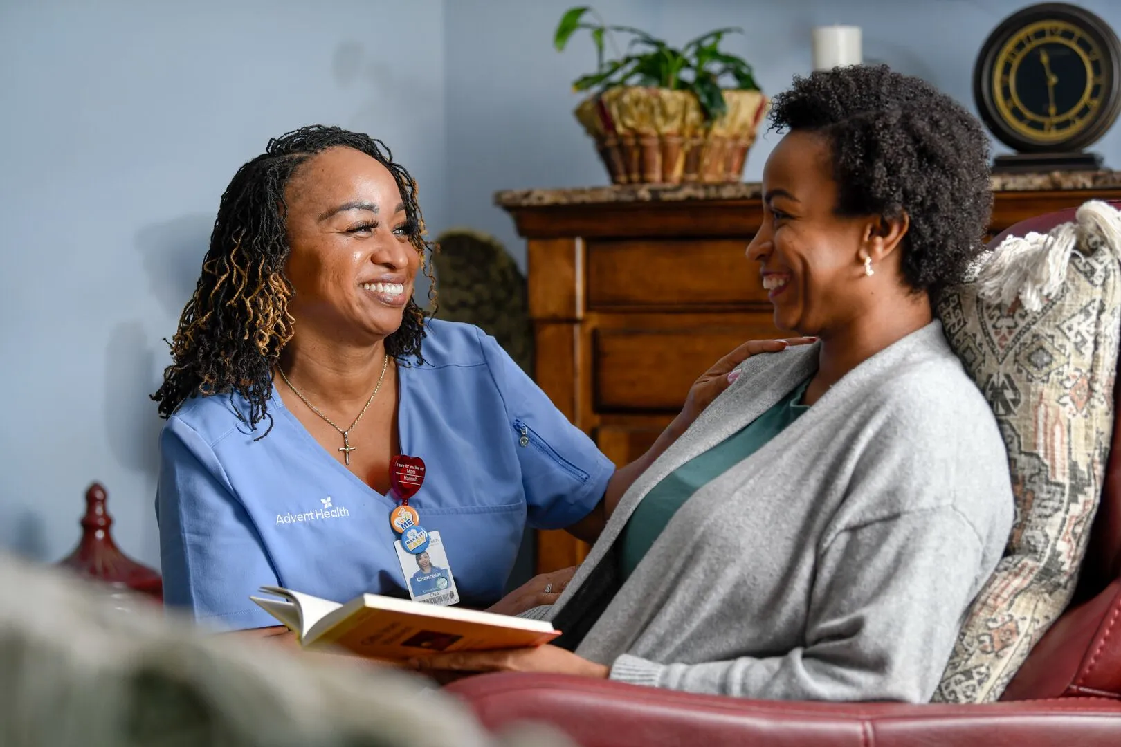AdventHealth nurse sitting with a patient, smiling and talking while holding a book in a comfortable home setting.
