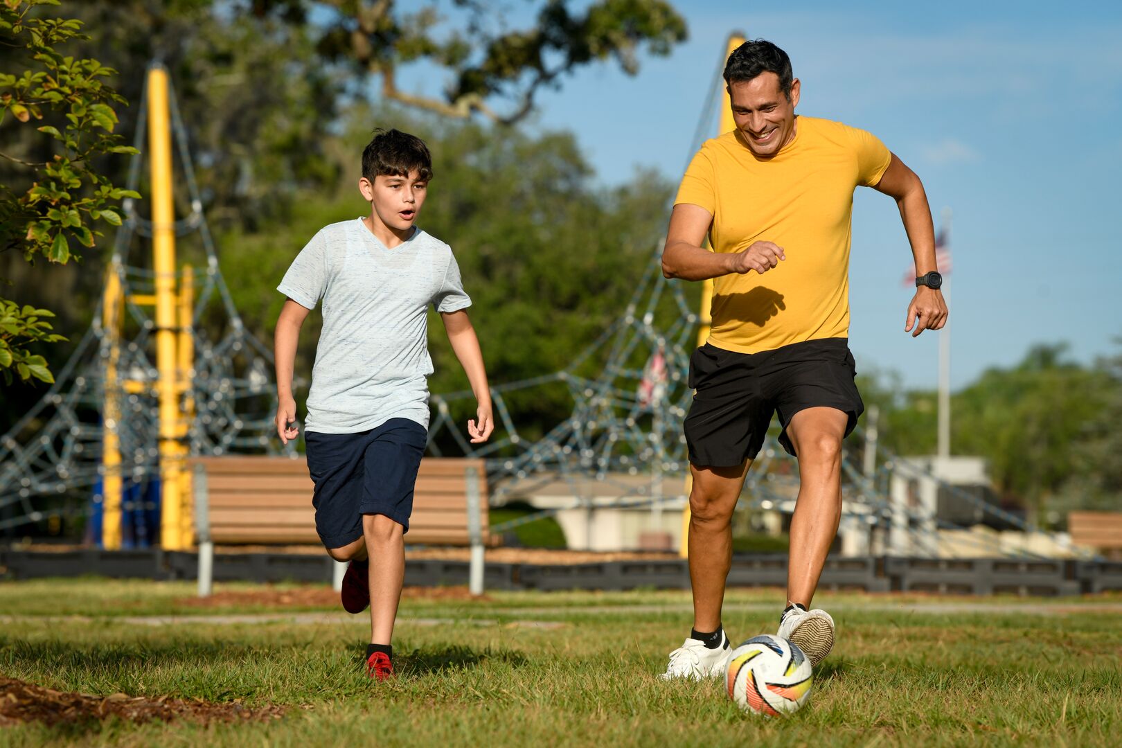 Son and father playing soccer in park