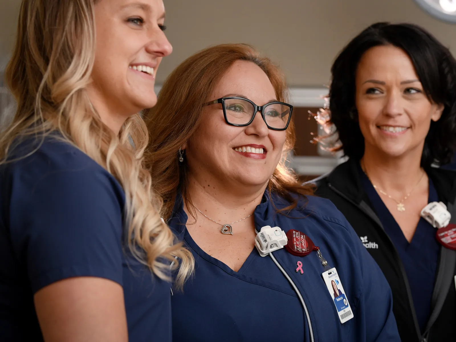 Three AdventHealth nurses smiling and talking together in a hospital setting.