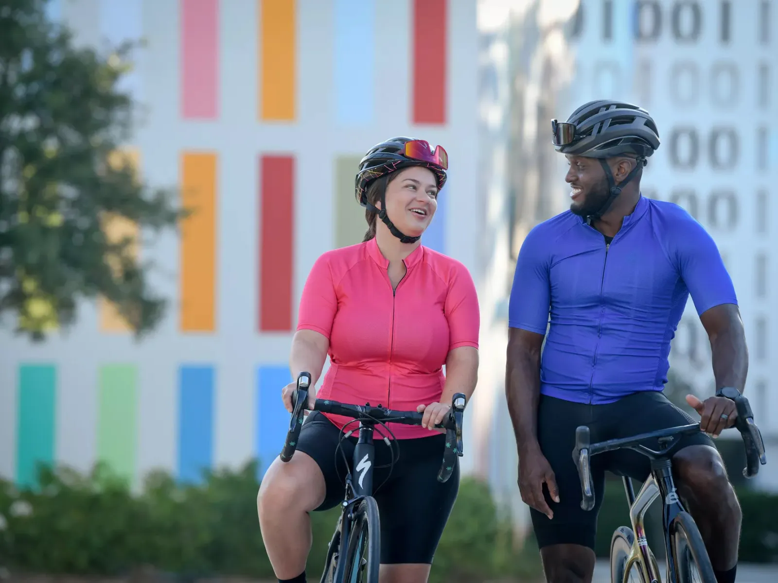 Two cyclists wearing helmets ride side by side and talk along a path in the Lake Nona community.
