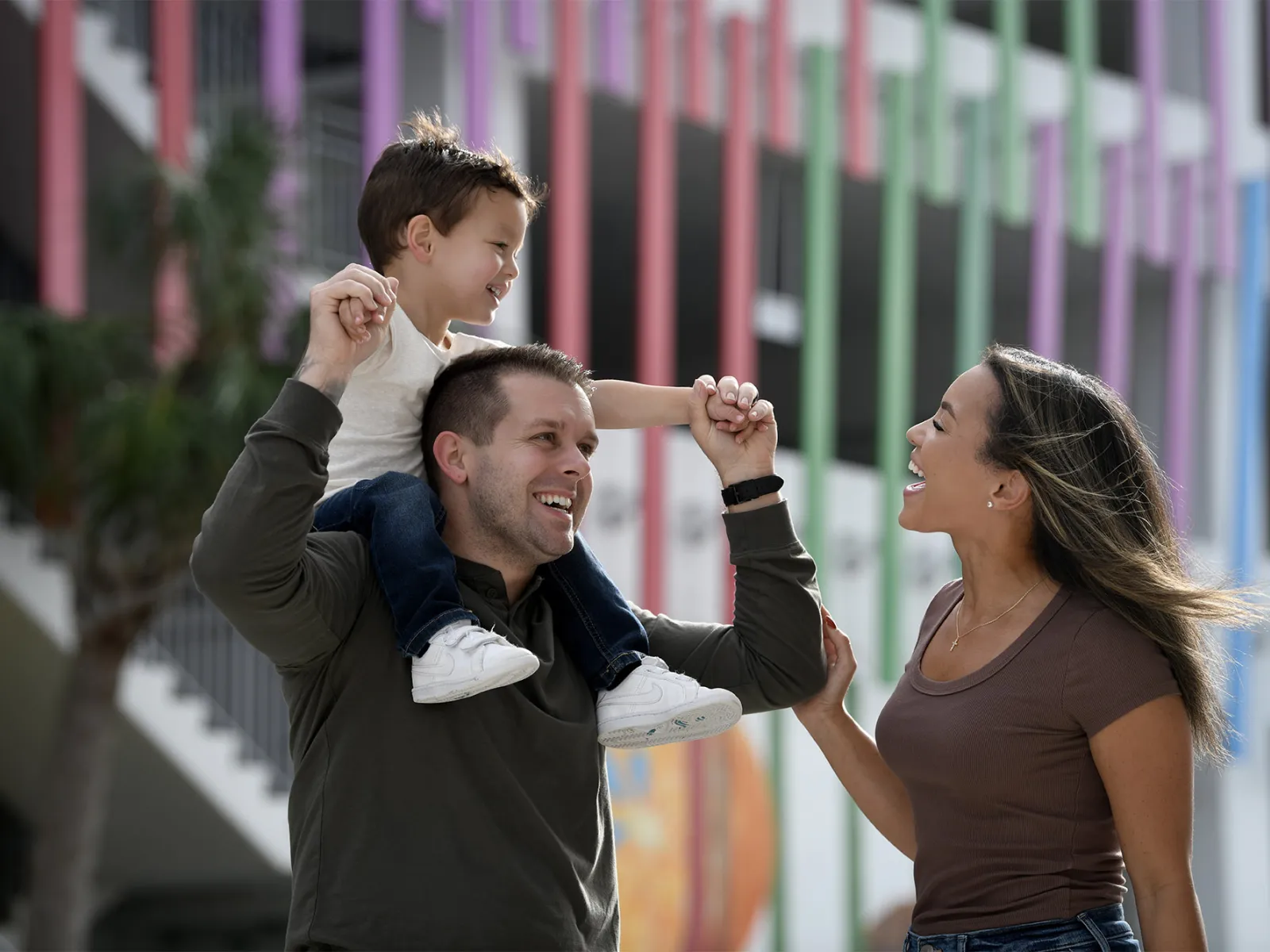A family smiles and walks together outdoors, with a parent carrying a child on their shoulders in the Lake Nona community.