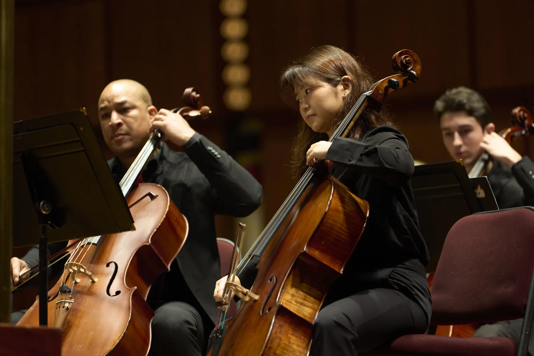 Three AdventHealth cellists performing on stage during an orchestral concert.