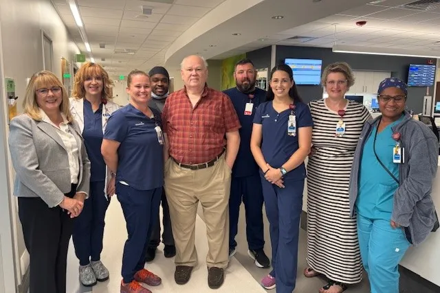 Patient standing with a group of hospital clinicians in an emergency department hallway.