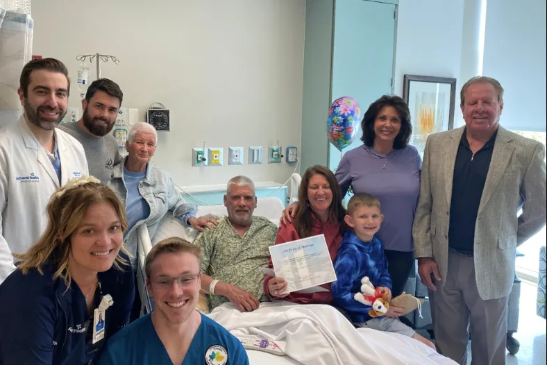 Hospital patient in a bed surrounded by family members and clinicians in a hospital room.