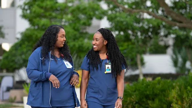 Two nurses walking outdoors and talking together.