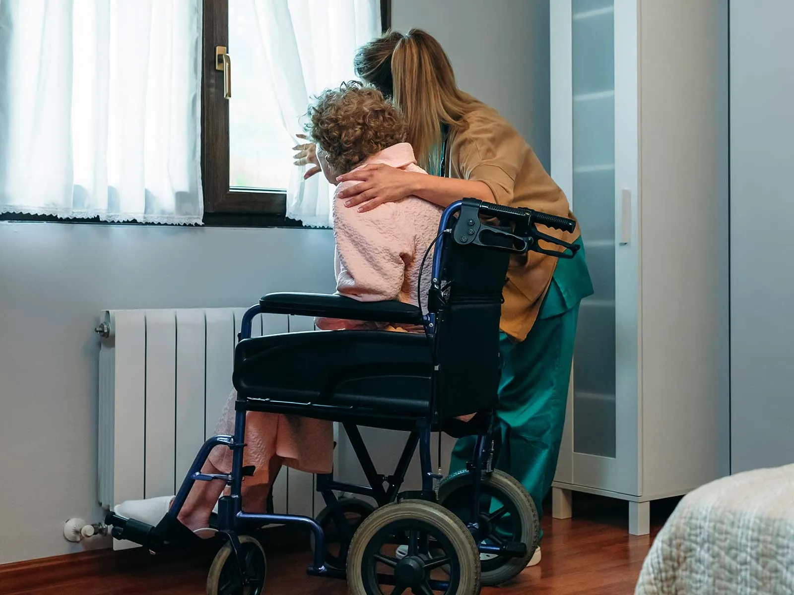 Caregiver helping a patient in a wheelchair look out the window.